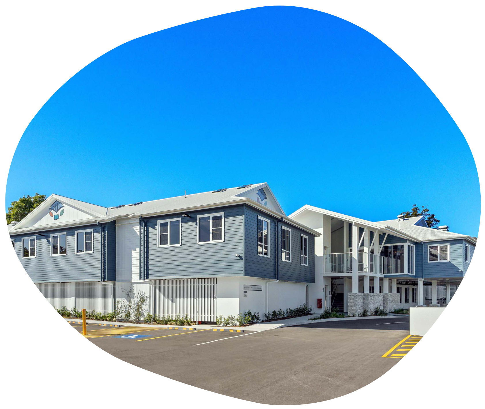 Blue and white two-story building with a parking lot and clear sky in a blue circle.