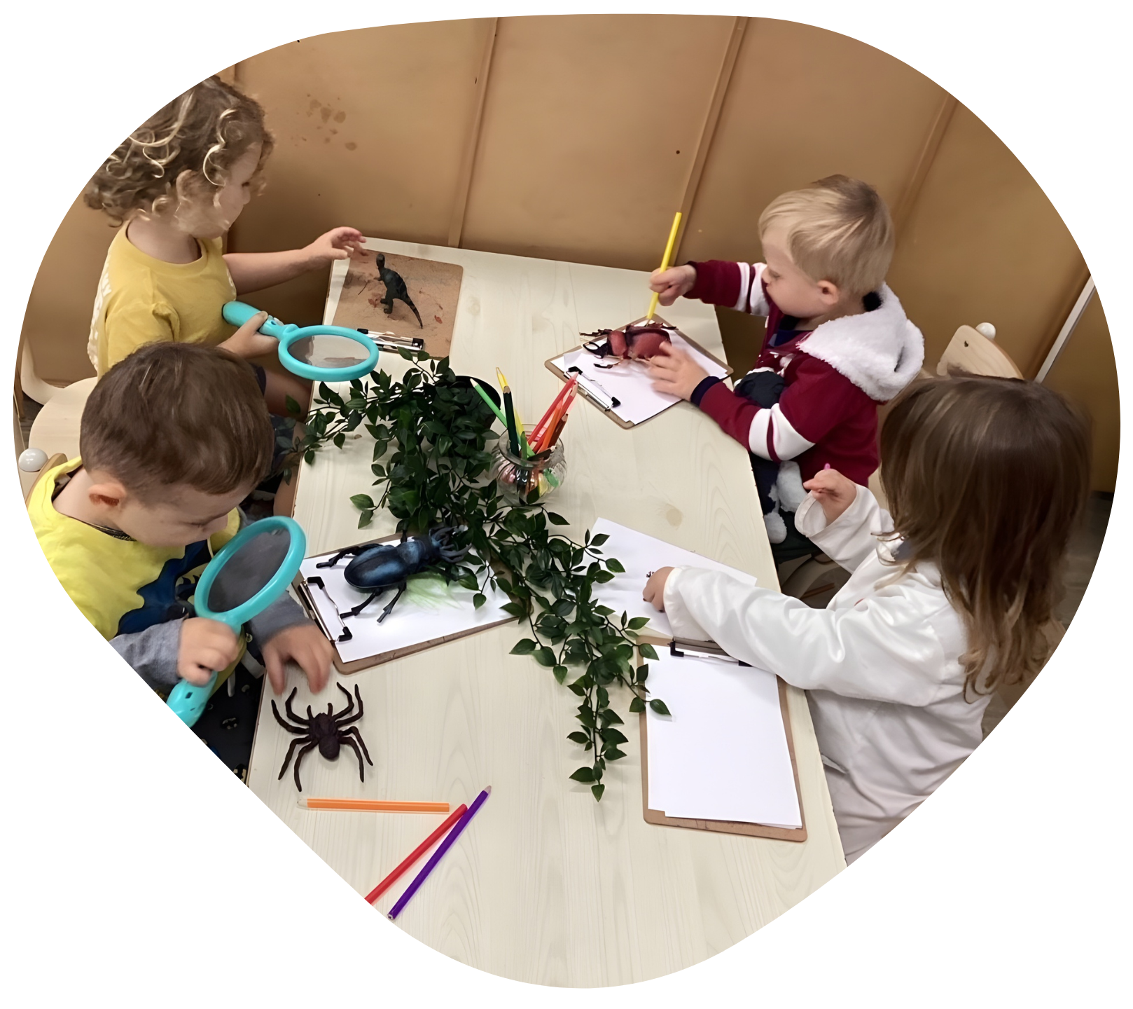 Children examining toy insects on a table with magnifying glasses and drawing supplies.
