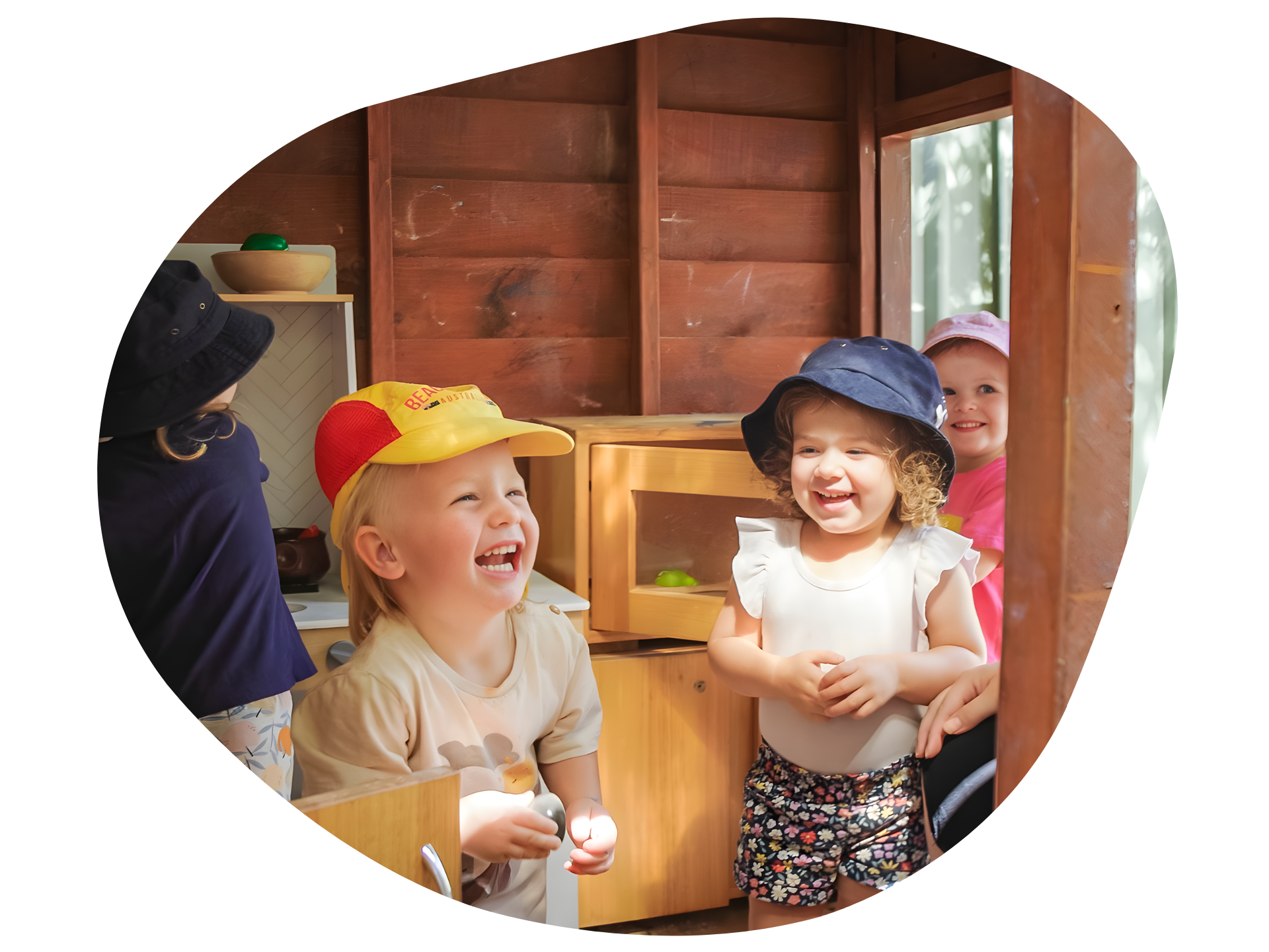Children laughing in a wooden playhouse, wearing hats, and enjoying themselves.
