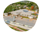 An aerial view of a daycare center with parking spaces and surrounding green trees.