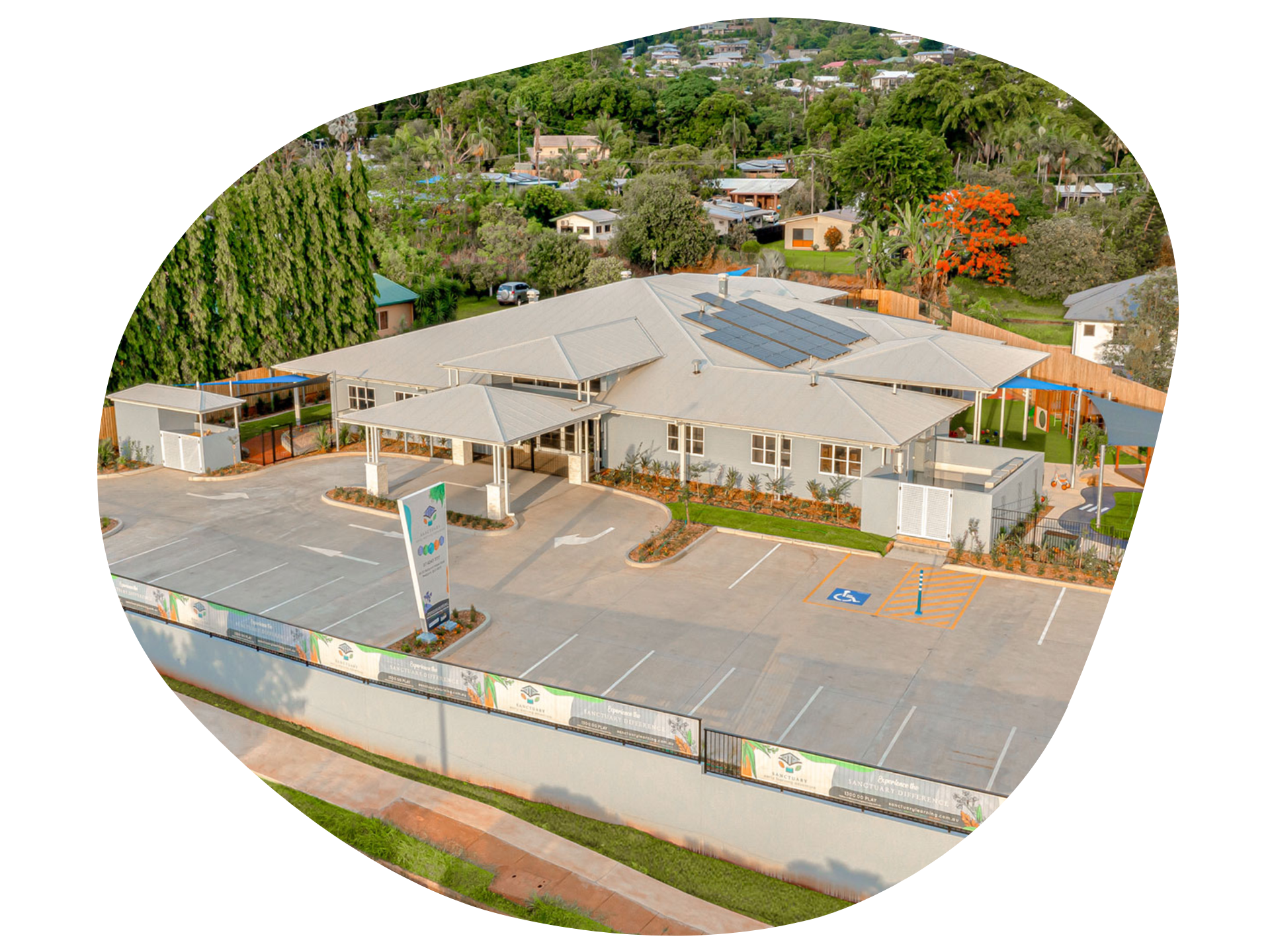 An aerial view of a daycare center with parking spaces and surrounding green trees.