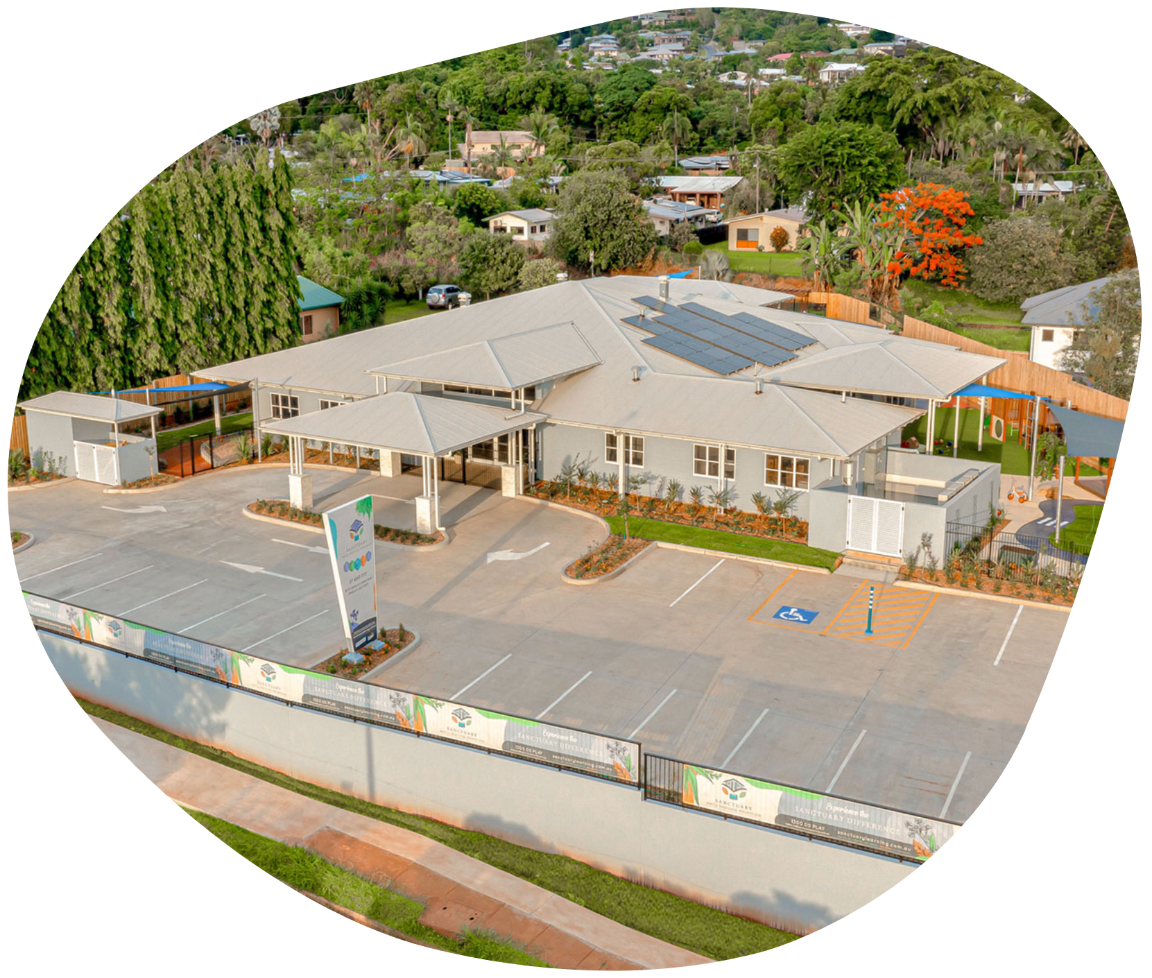 Aerial view of a light-colored building with solar panels, a parking lot, and surrounding greenery.