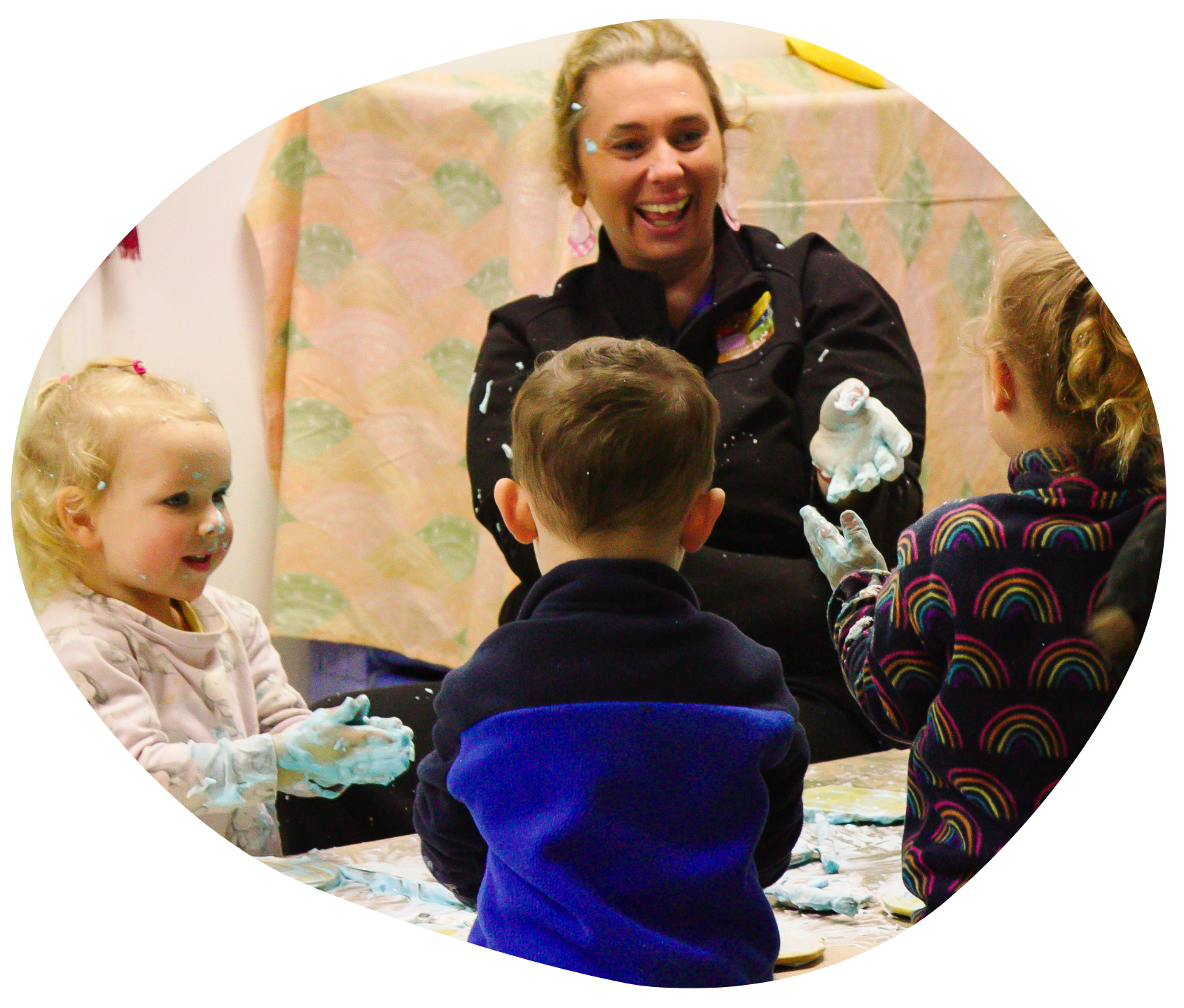 Children with blue paint on hands playing with an adult who is laughing.