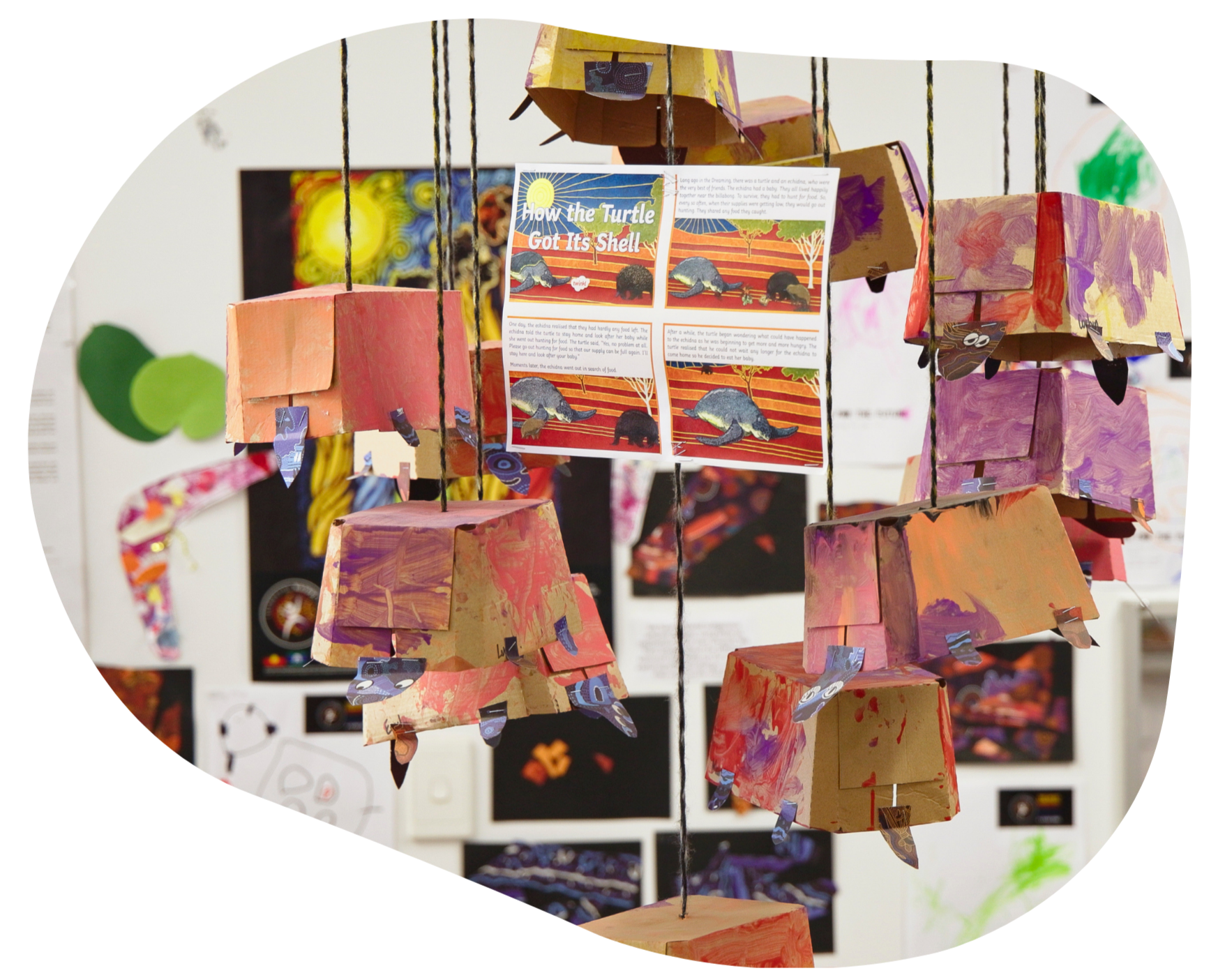 Display of hanging paper box art, colorful, with drawings on the wall in the background.
