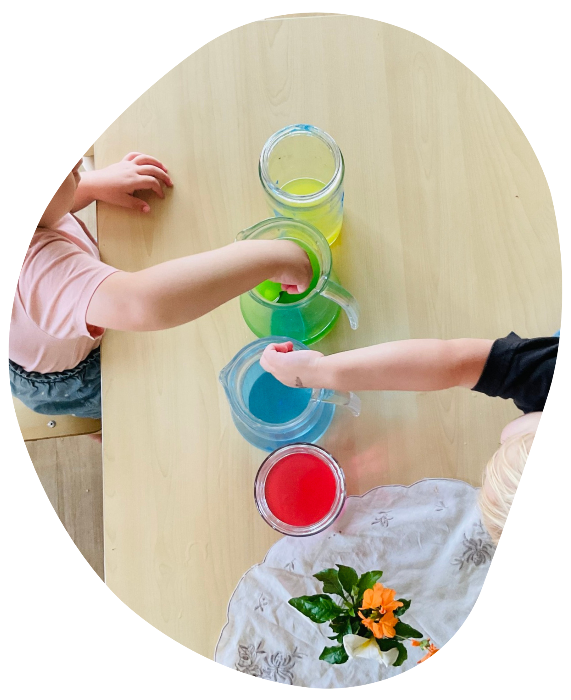 Children's arms reaching into jars filled with colorful liquids on a table.