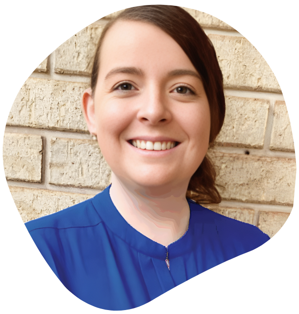 Woman with brown hair in blue shirt smiling in front of a brick wall.