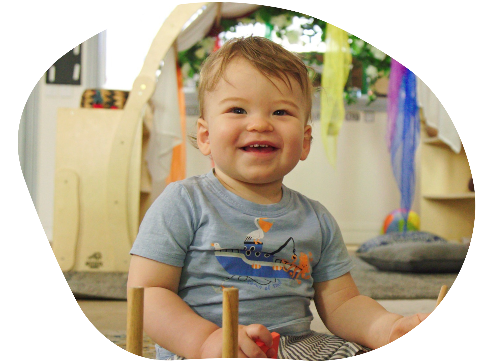 Smiling toddler in blue shirt playing with wooden toys.