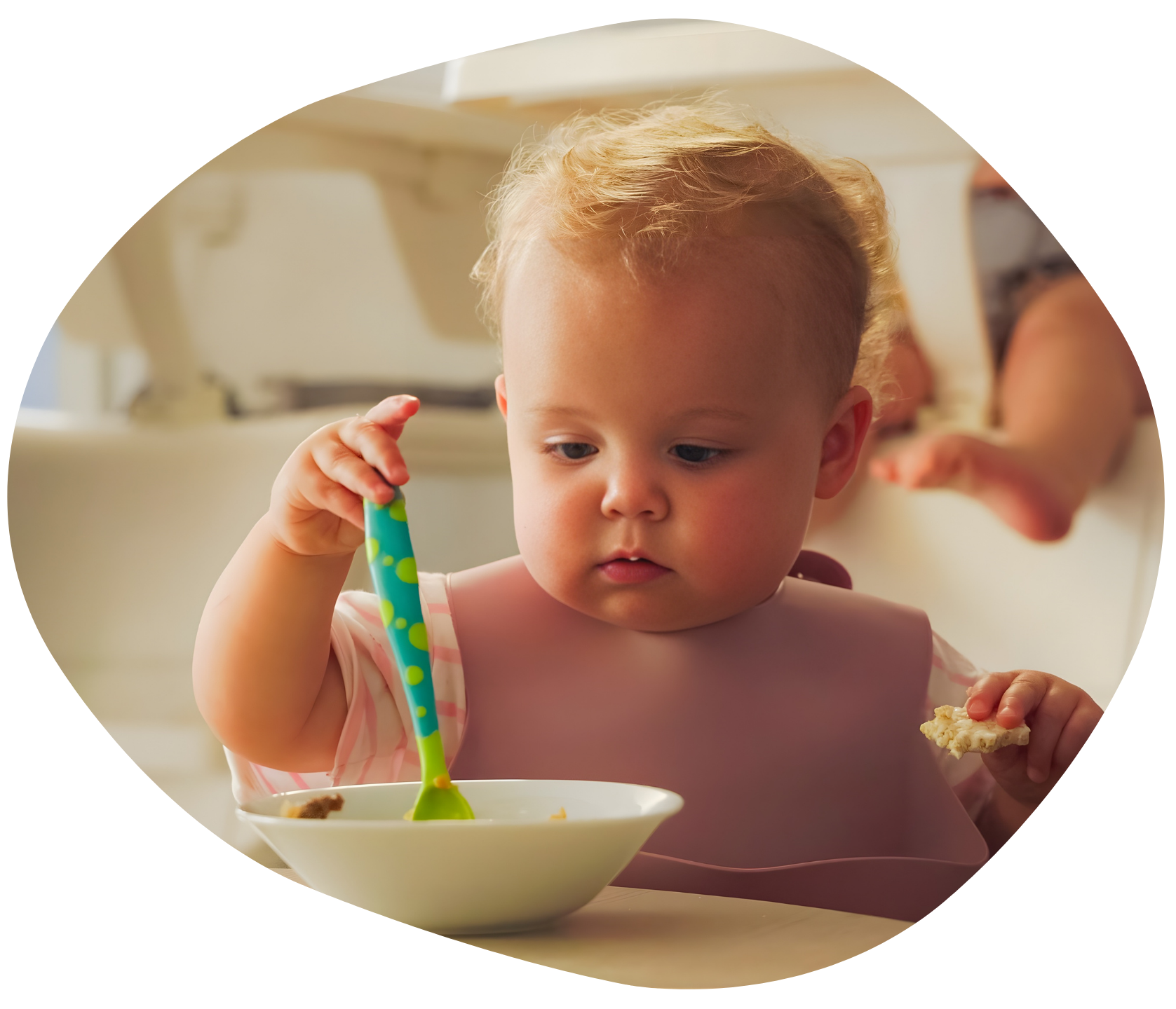 Baby in high chair eating from a bowl with a spoon. Wearing a pink bib.
