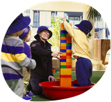 Children and adult building tower with large blocks in outdoor setting.