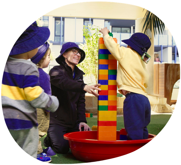 Children and adult building tower with large blocks in outdoor setting.