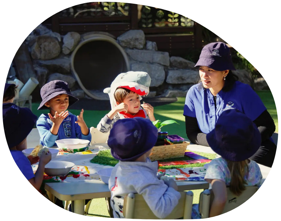 Children in blue hats, teacher, outdoor table, tunnel, eating, playing.