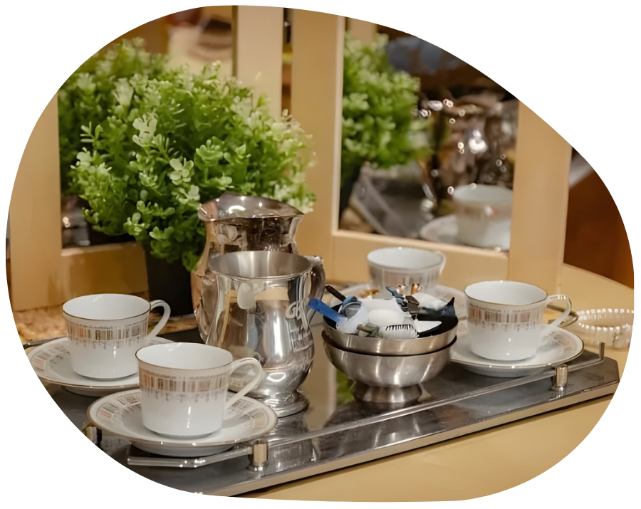 Tea set on a tray, including cups, saucers, creamer, sugar bowl, and a plant in front of a mirror.