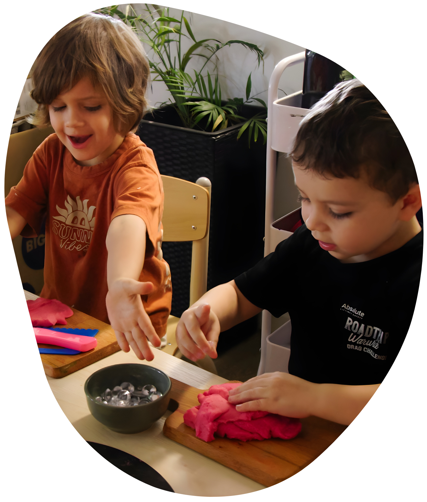 Two children playing with pink playdough at a table. One smiles, the other concentrates.