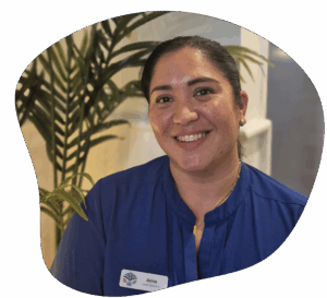 Woman in blue shirt smiling, with leafy plant in the background.