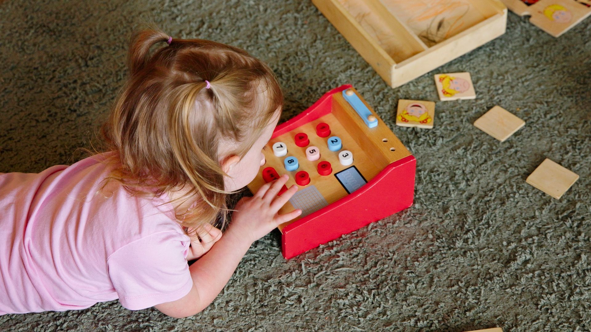 Child laying on the ground playing with a toy cash register.