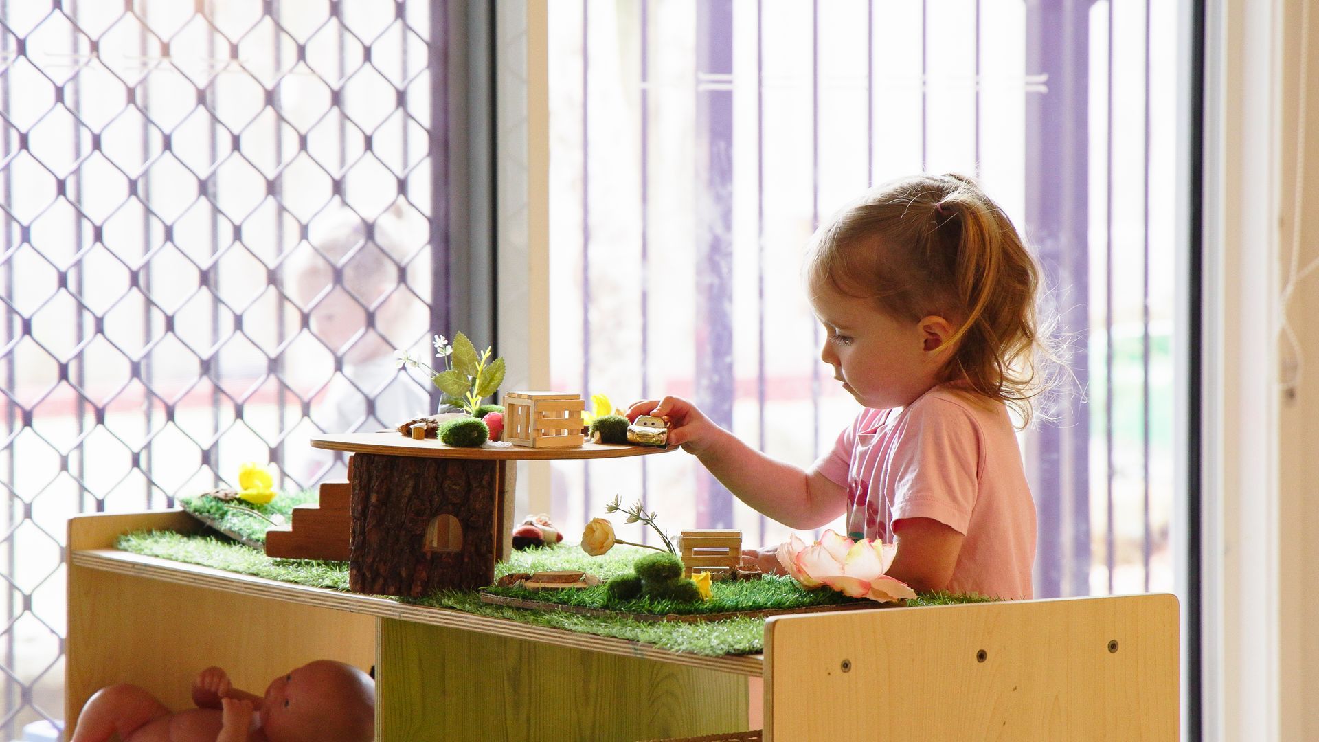 Young child playing with small wooden toys on a tabletop, inside near a window.