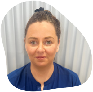 Woman with brown hair in a bun, wearing a blue shirt, smiling in front of a white curtain.