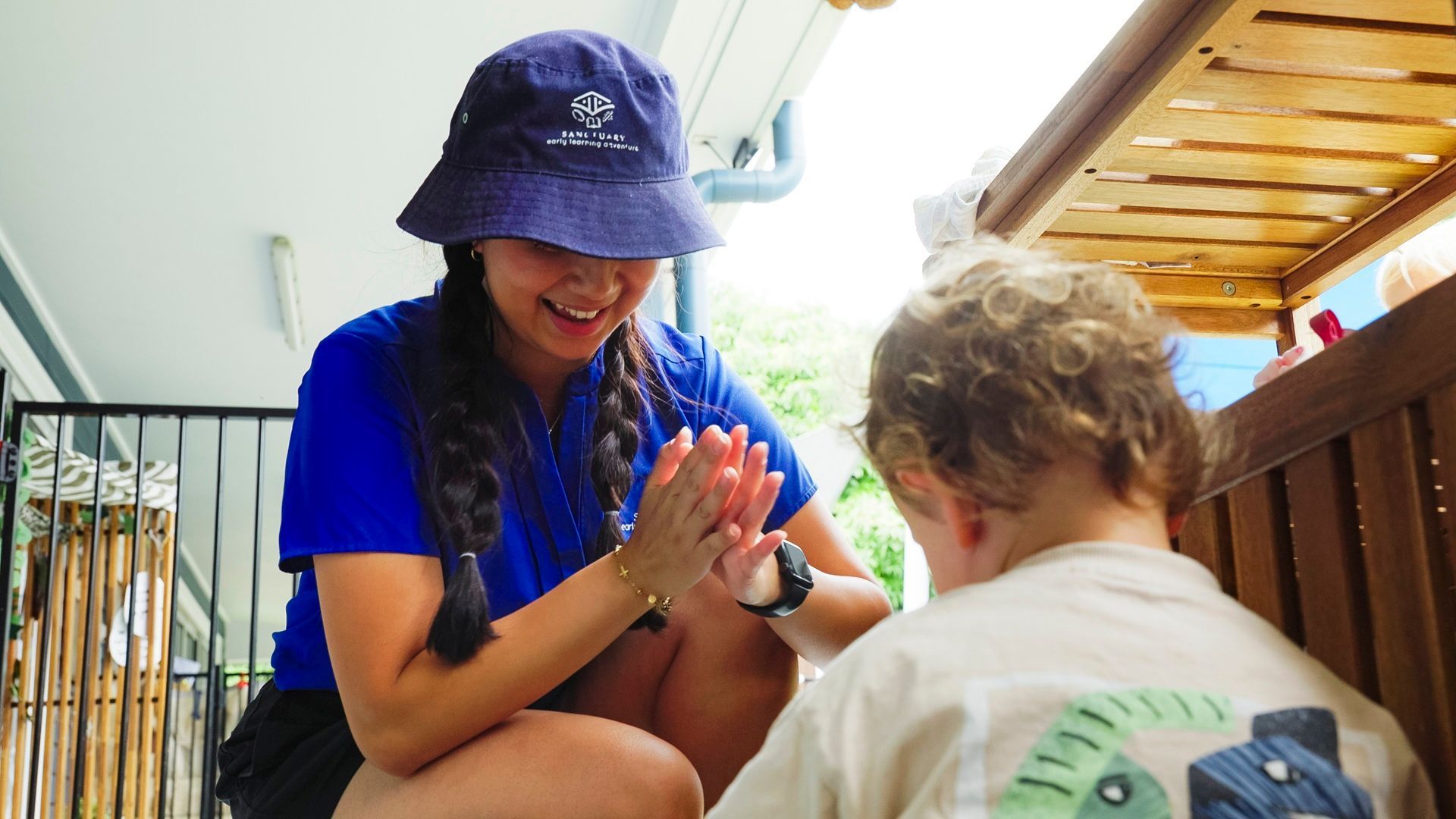 smiling educator crouches beside child to help with their shoe
