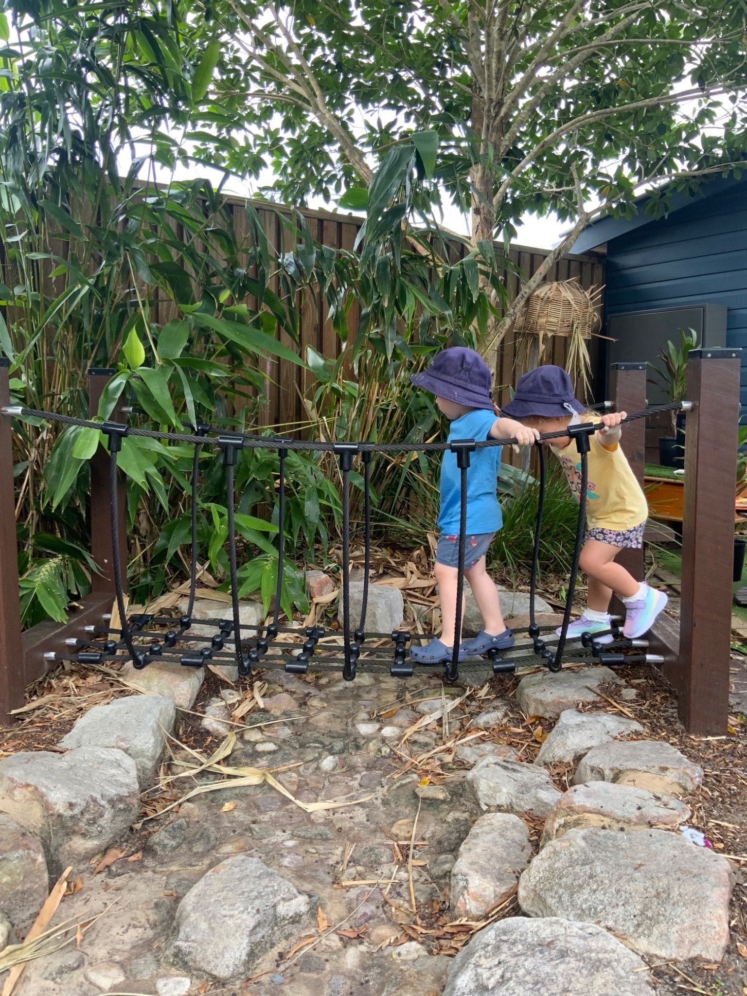 Two children walk across  bridge in a child care centre