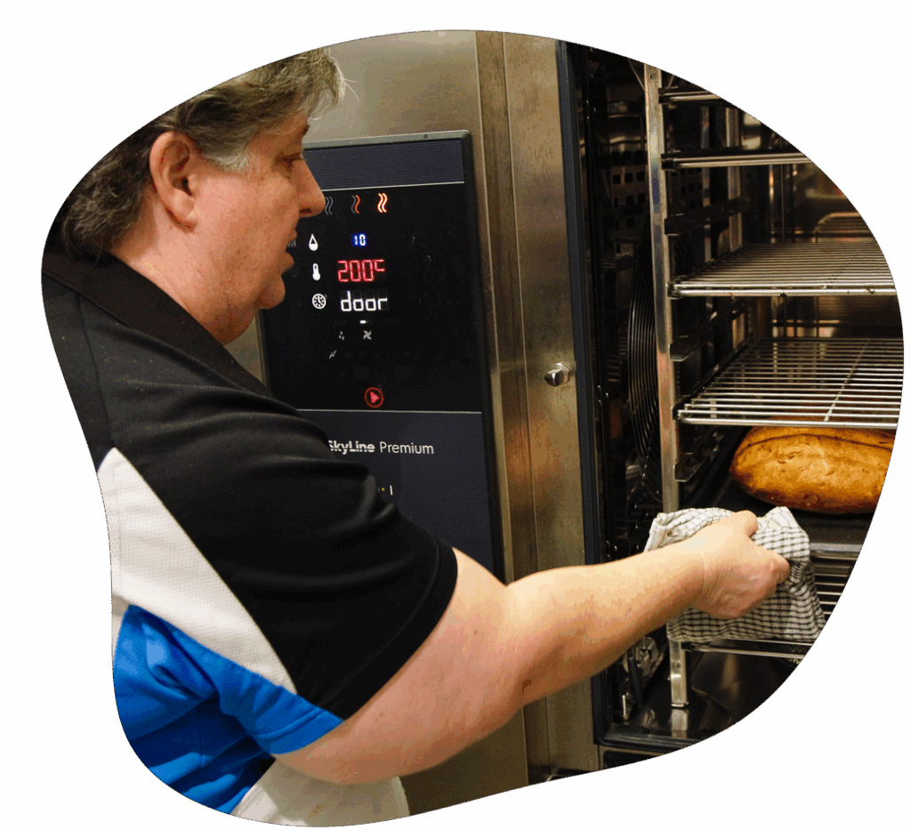 Man in a black and blue shirt removing a loaf of bread from a commercial oven.