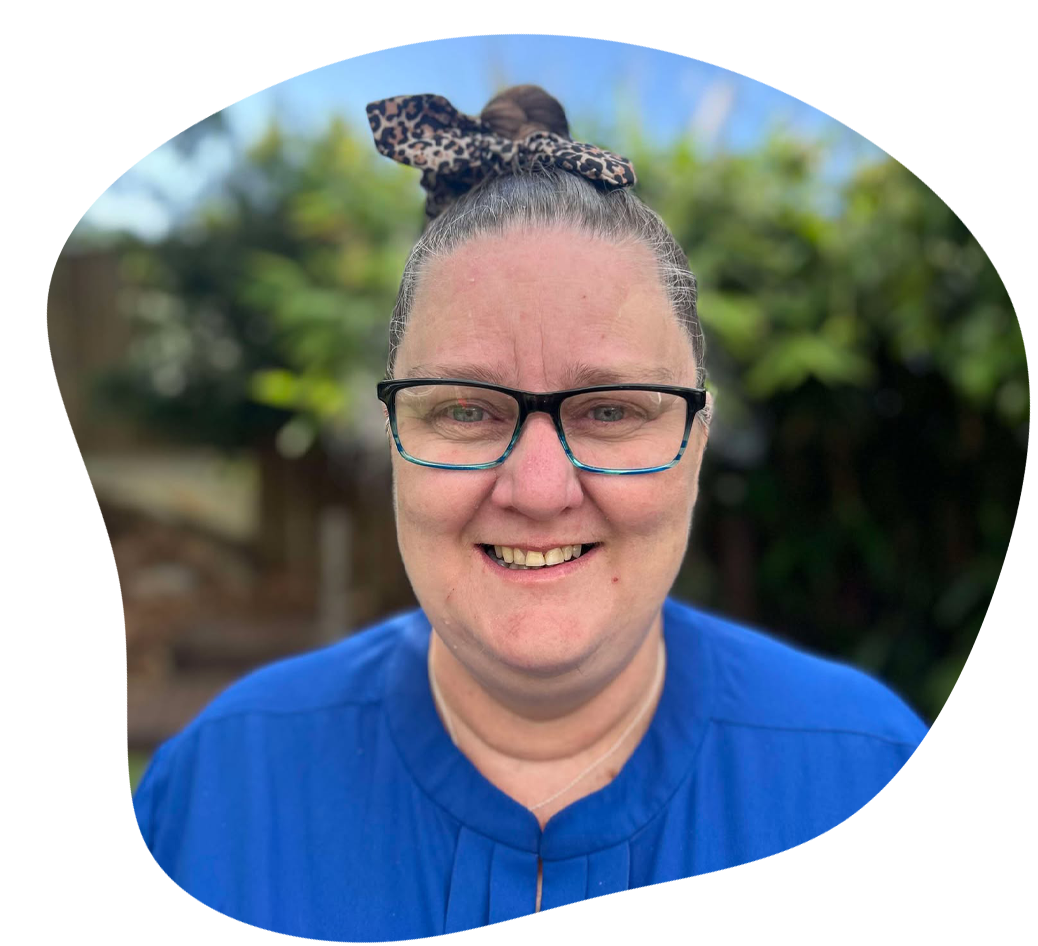 Woman with glasses and bun, wearing blue shirt, smiling outdoors.