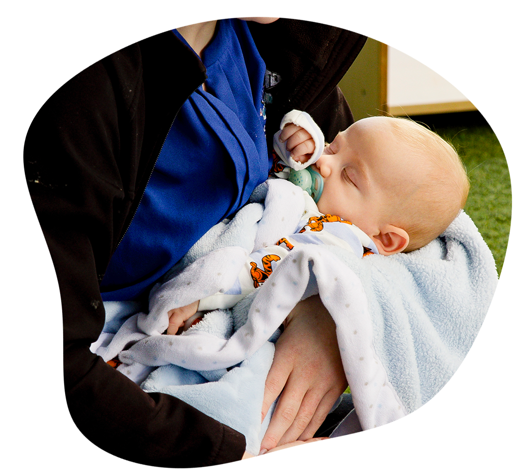 Sleeping baby being held by educator, wrapped in blanket with a dummy