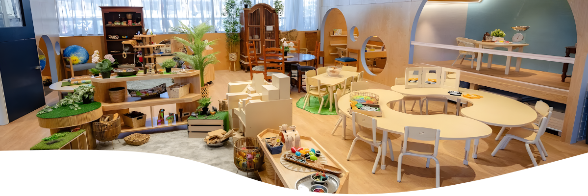 A well-lit, natural-toned playroom with wooden furniture, toys, and tables.