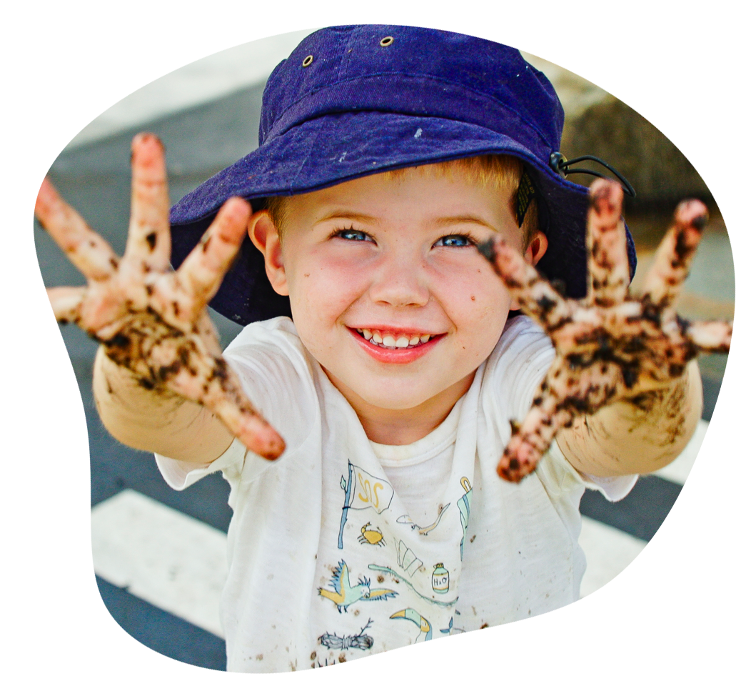 Smiling child with dirty hands wearing a blue hat, white shirt, outdoors.
