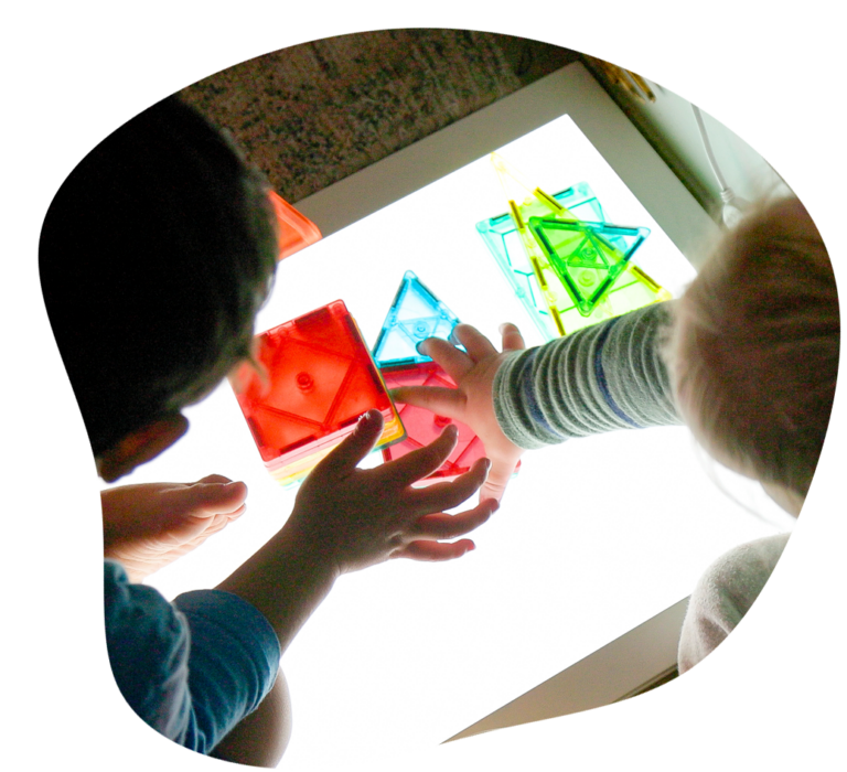 Two children playing with colorful translucent shapes on a light table.