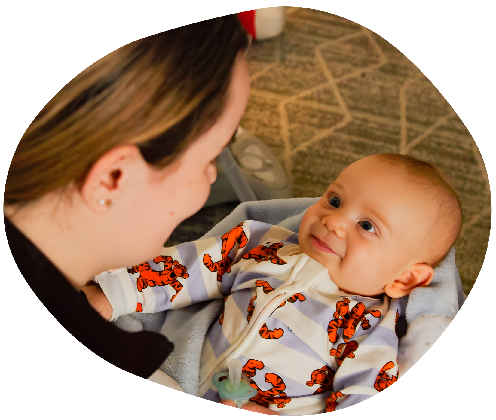 Woman gazing at smiling baby in patterned onesie, indoors.