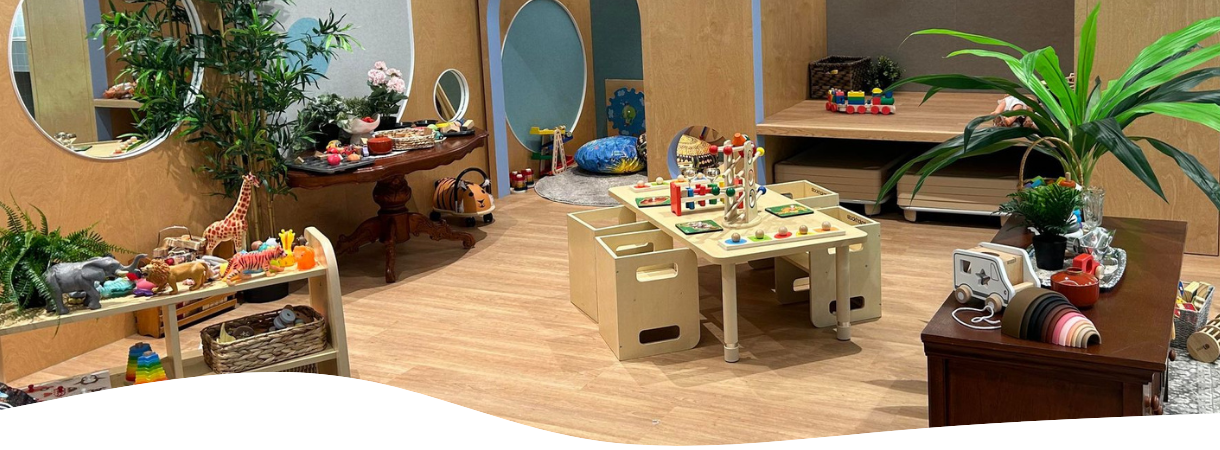 Interior of a room, possibly a child's playroom. Features toys, plants, a table, and shelves.