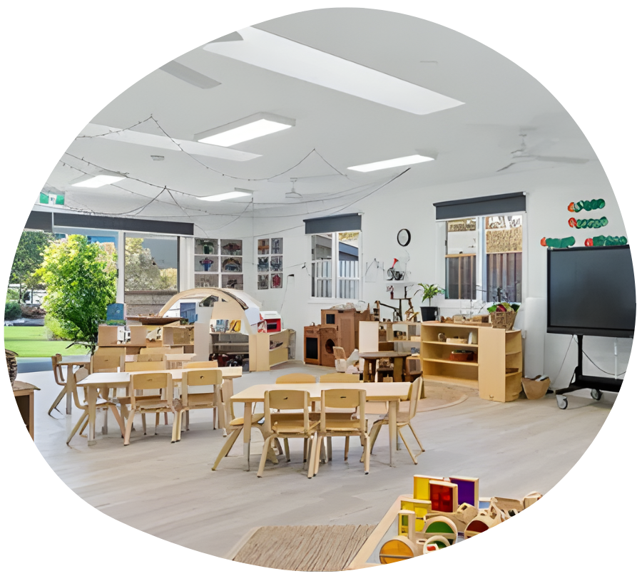 Kindergarten classroom with tables, chairs, learning stations, and a large screen.