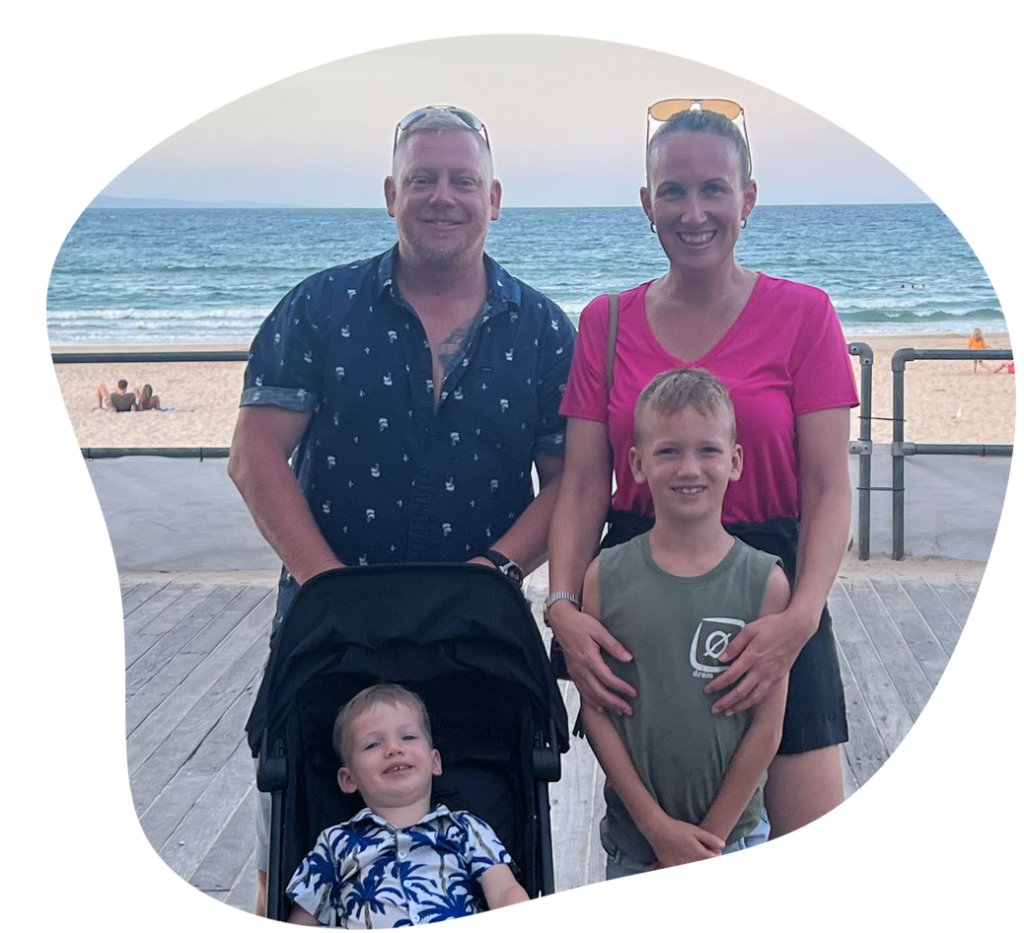 Family posing on a boardwalk near a beach; two adults, two children.