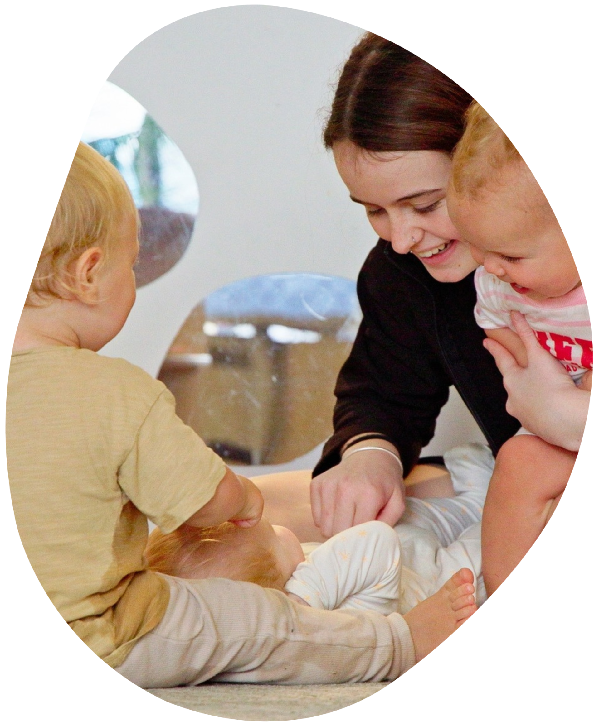 Two toddlers playing with a jar and spatula at a table indoors. One smiles.