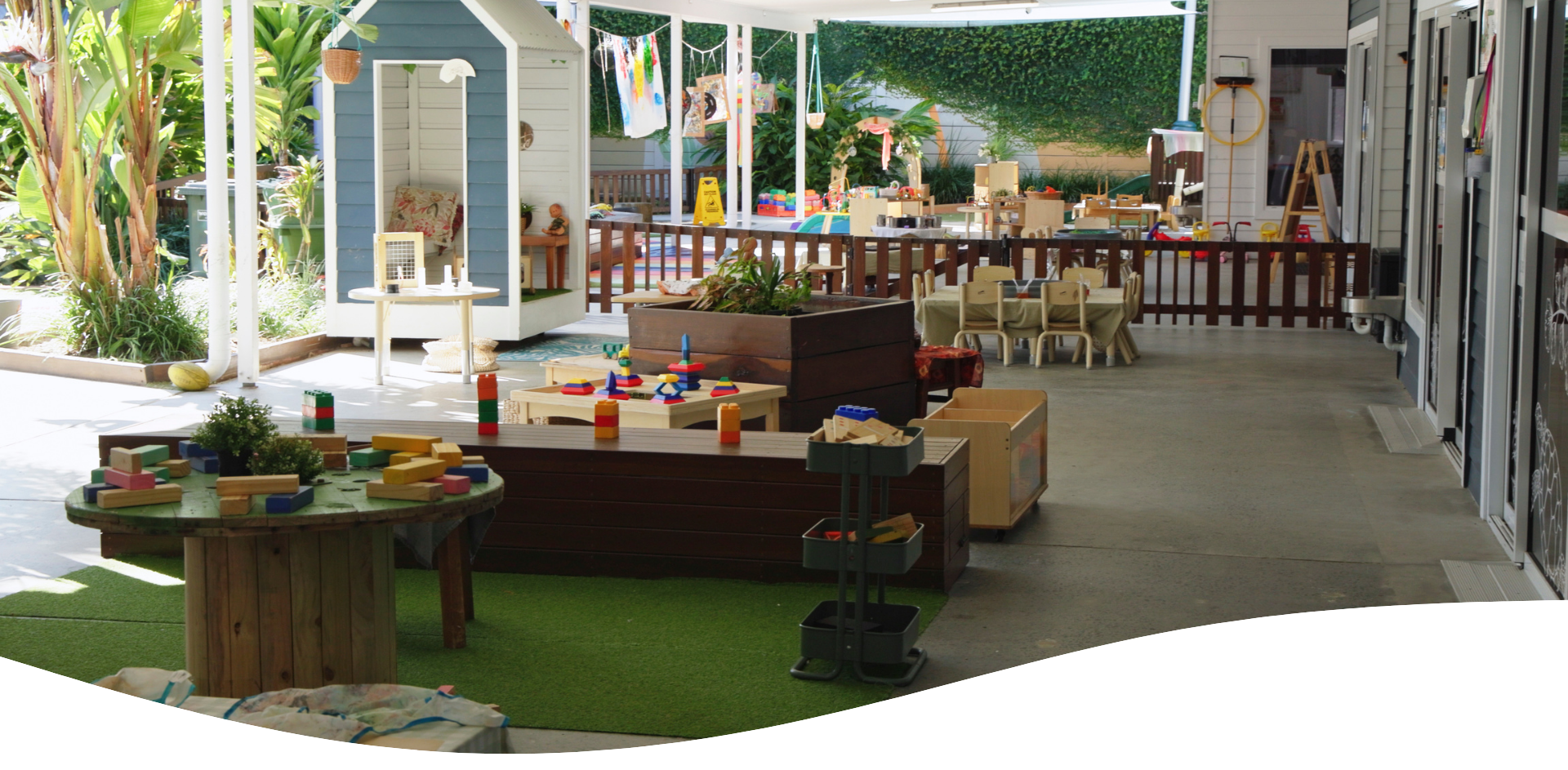 Outdoor preschool classroom with playhouse, tables, and toys.
