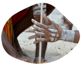 Hands with white paint, turning a wooden drill in sand.