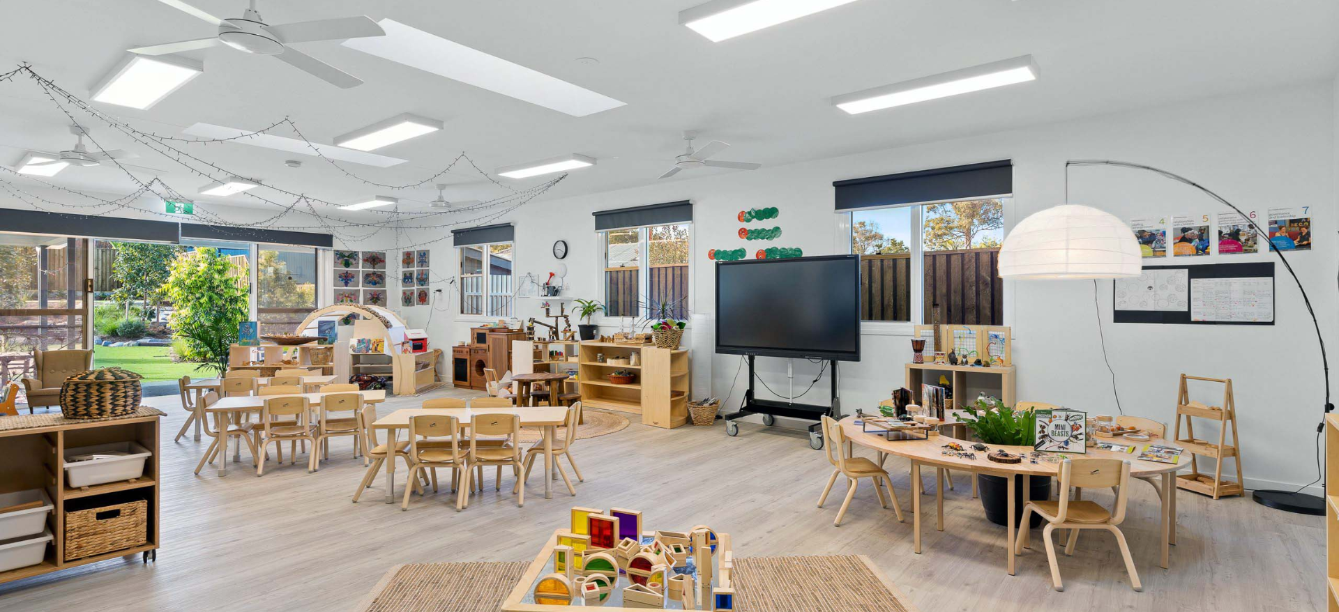 A well-lit preschool classroom with tables, chairs, and learning materials.