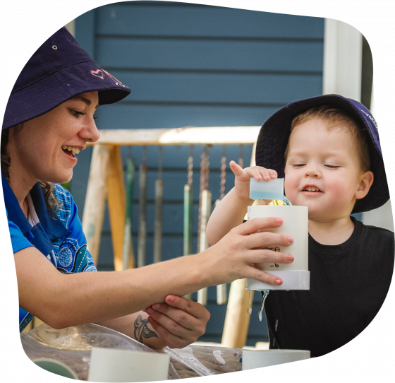 Girl with bucket hat examines stone with magnifying glass; smiling.