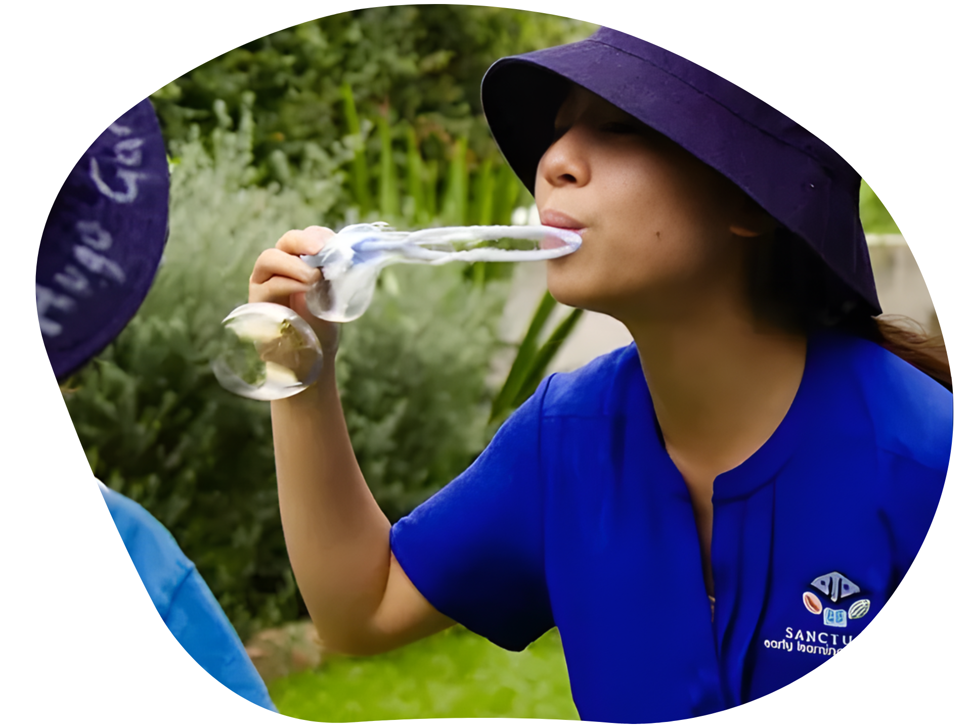 Woman in blue shirt blowing a bubble from a wine glass, wearing a sun visor outdoors.