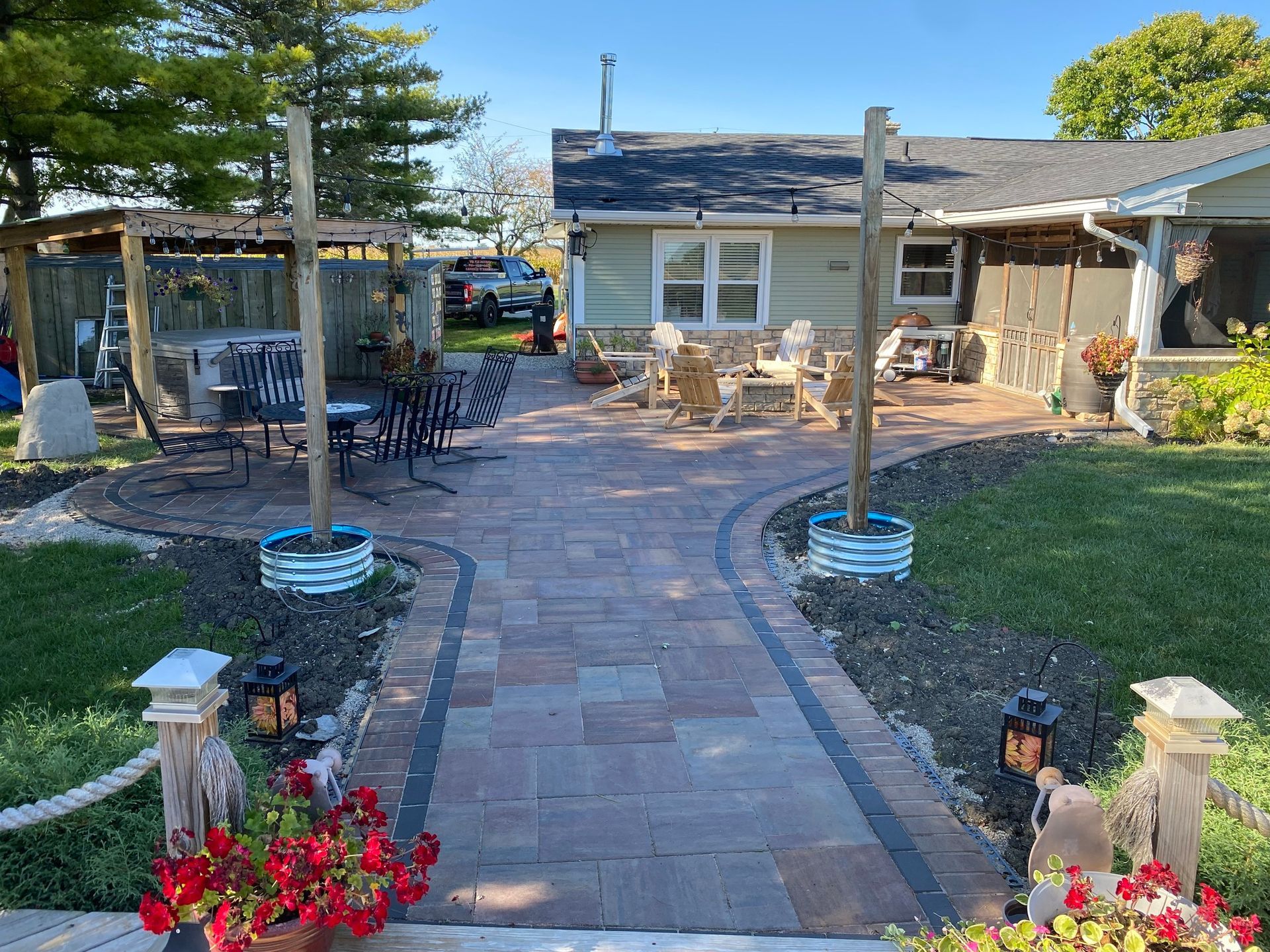 Brick patio with seating areas, leading to a house. Flowerbeds flank the walkway.