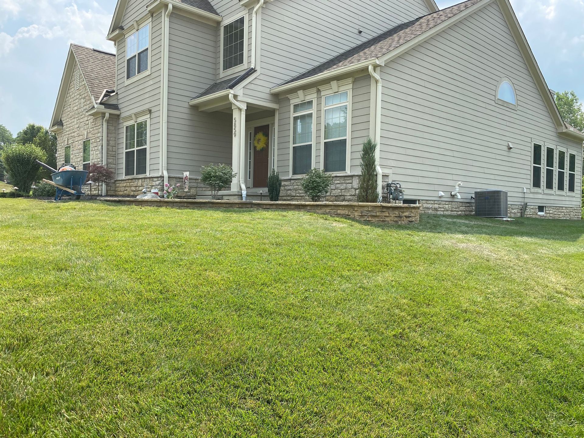 Two-story beige house with a well-manicured lawn and stone accents.