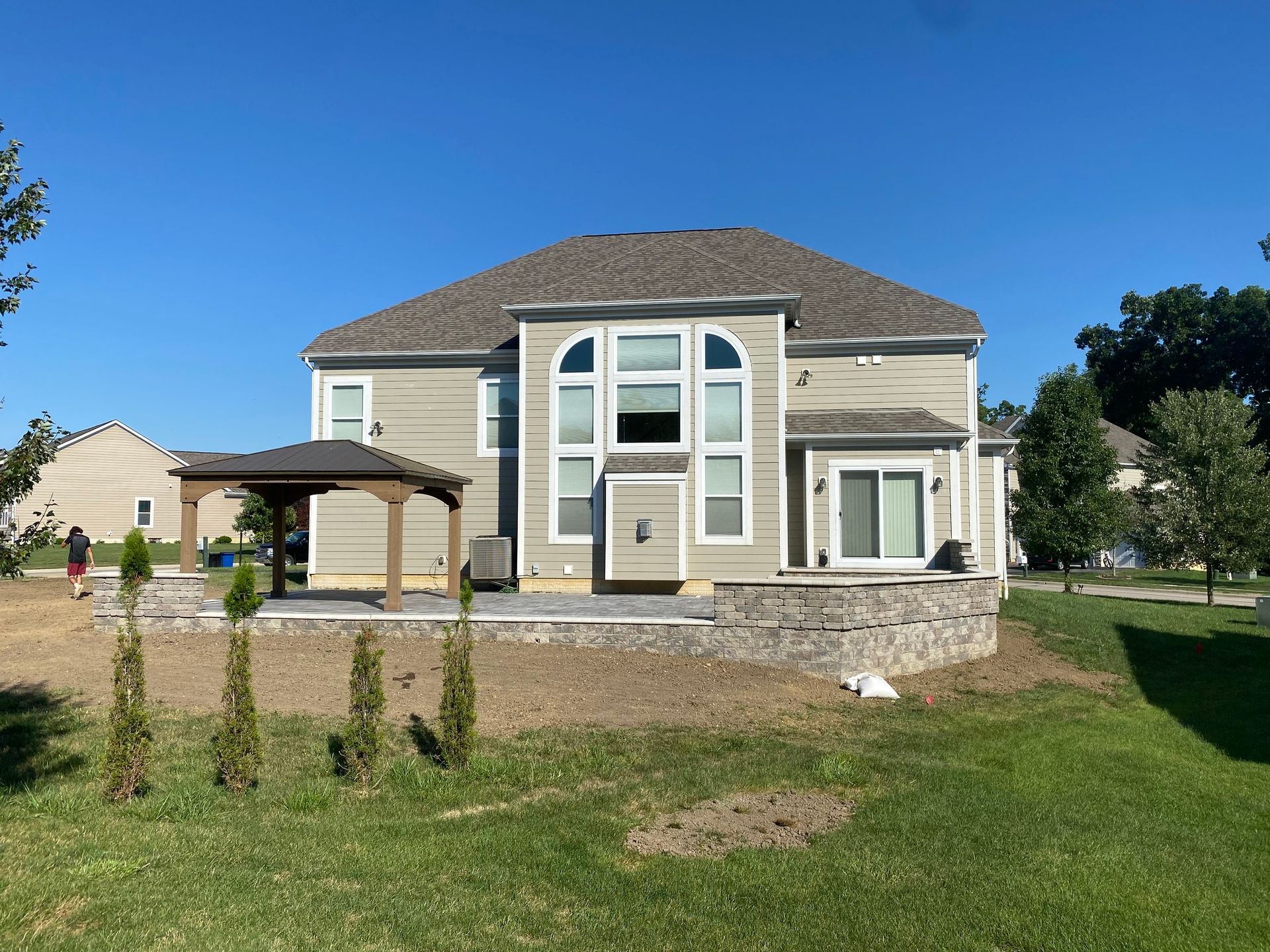 Tan house with stone patio, pergola, and young trees on a sunny day.