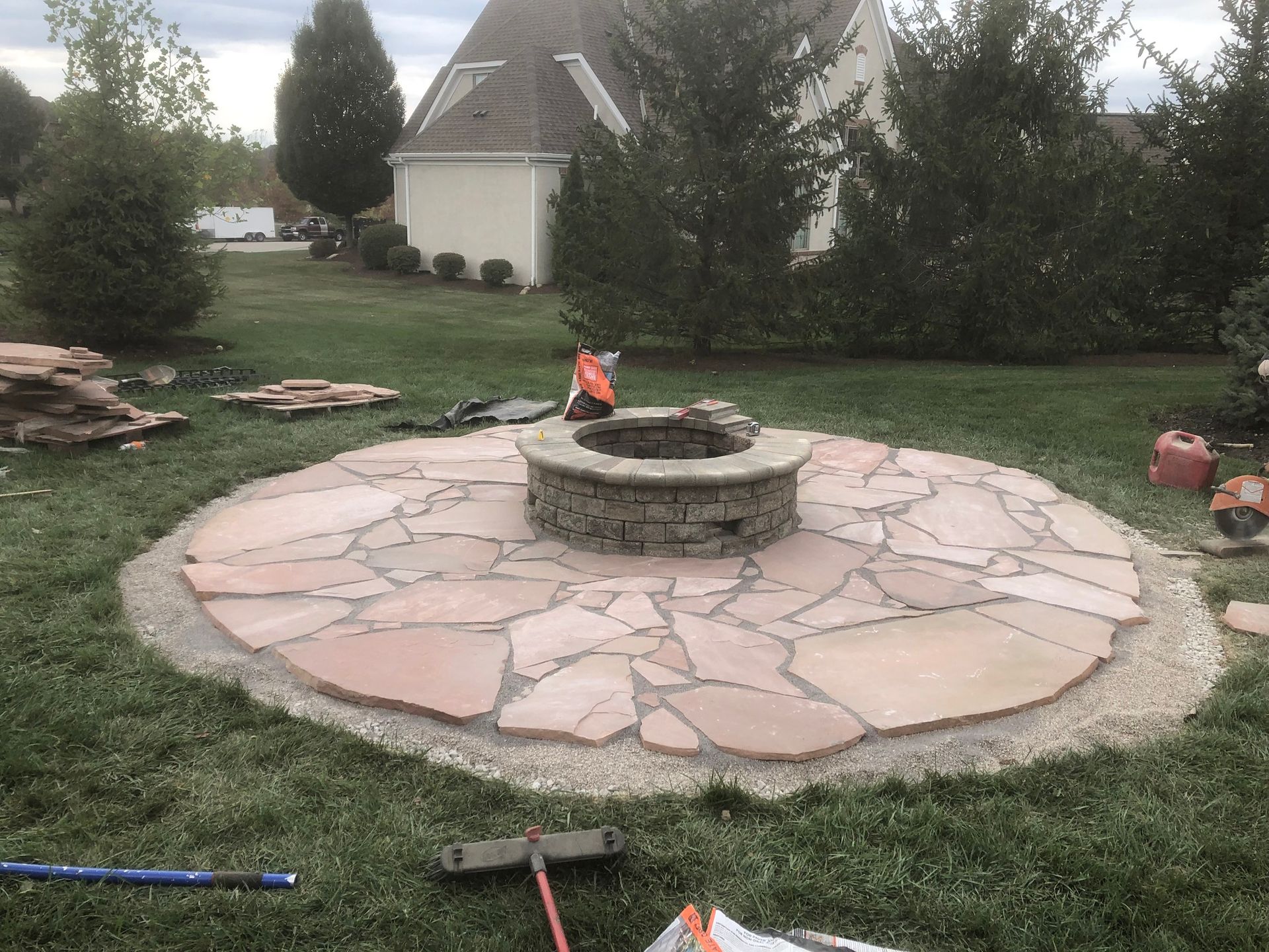 Circular stone patio with fire pit, surrounded by gravel and grass.