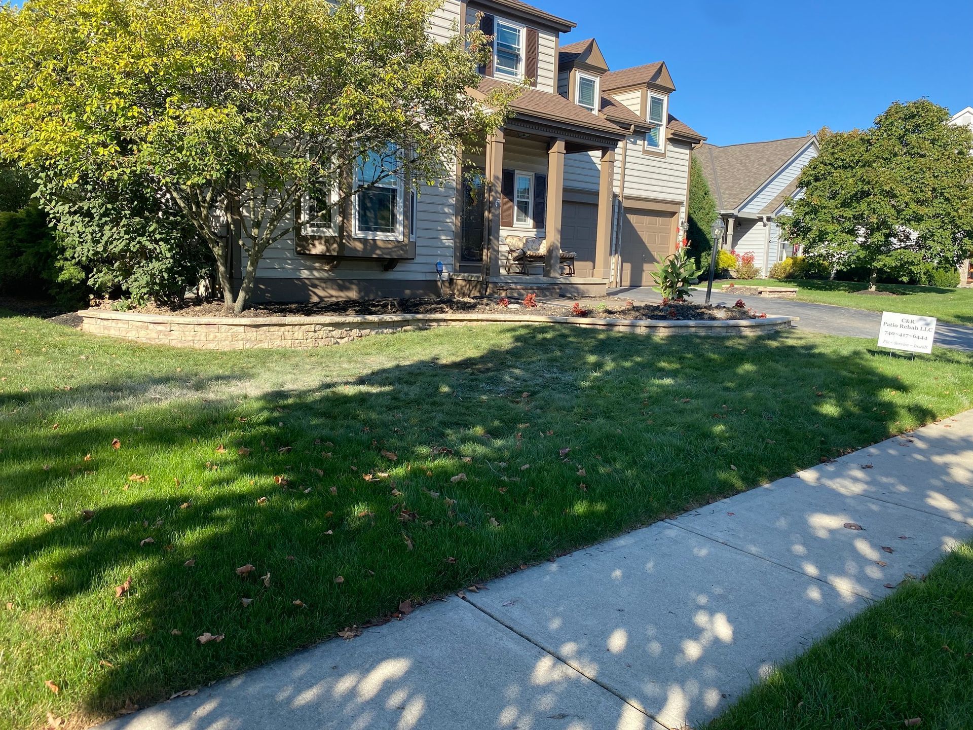 House with a green lawn, brick border, and a sidewalk in front. Sunny day.