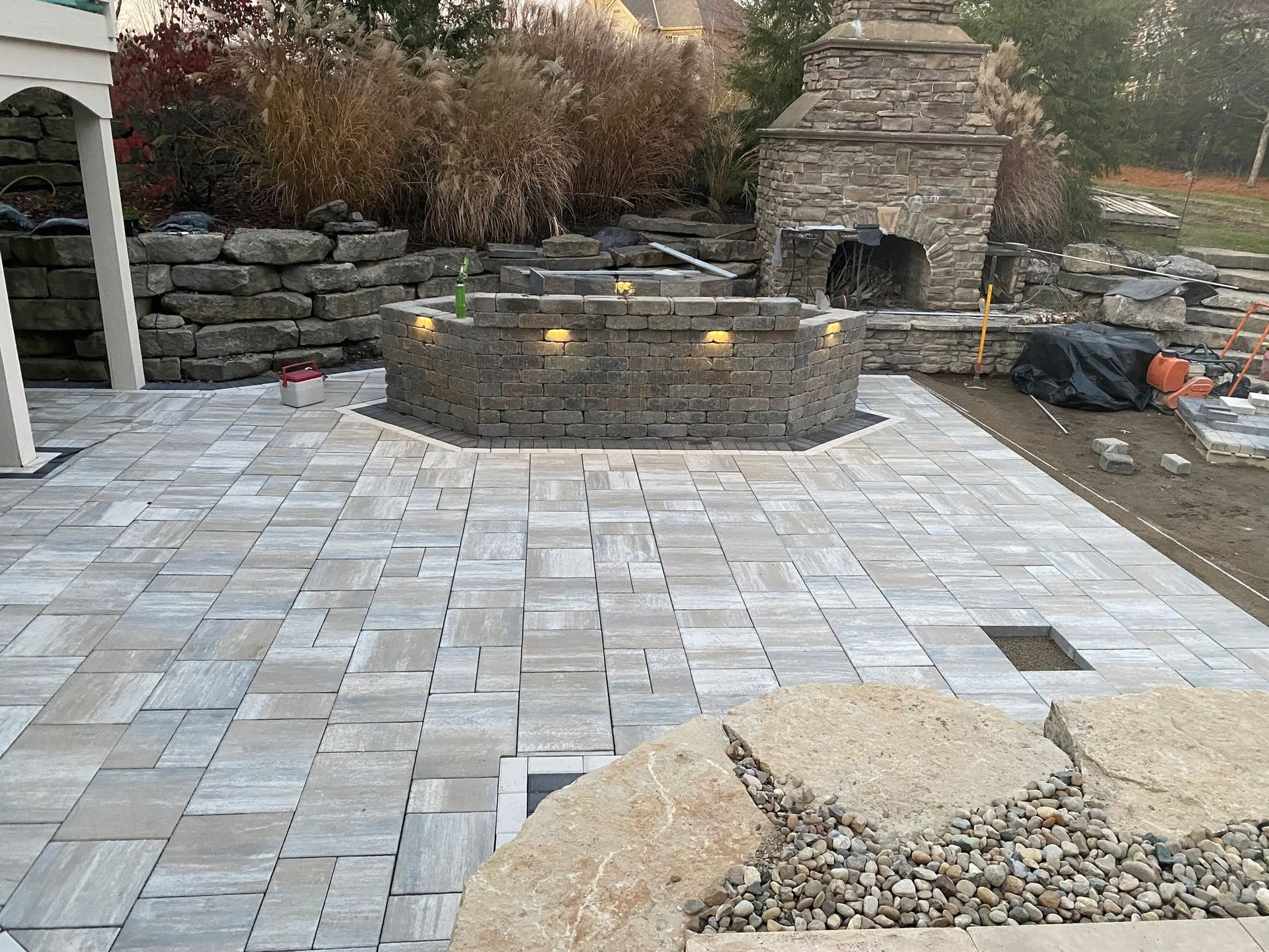 Stone patio with built-in fire pit, stone fireplace, and retaining wall in an outdoor setting.
