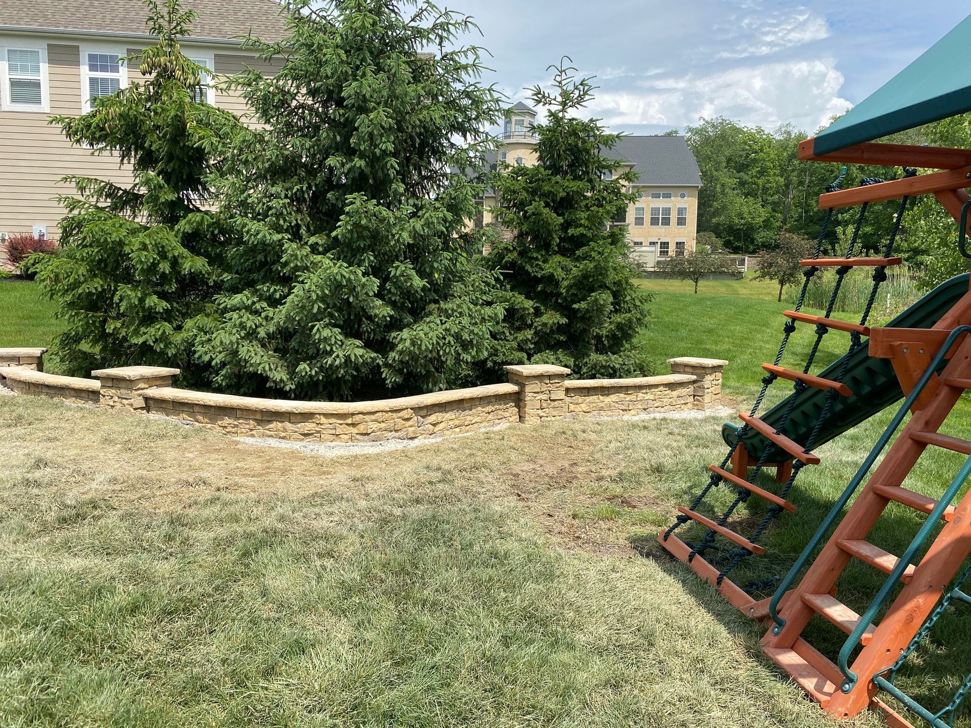 Backyard with retaining wall, trees, and children's play set.