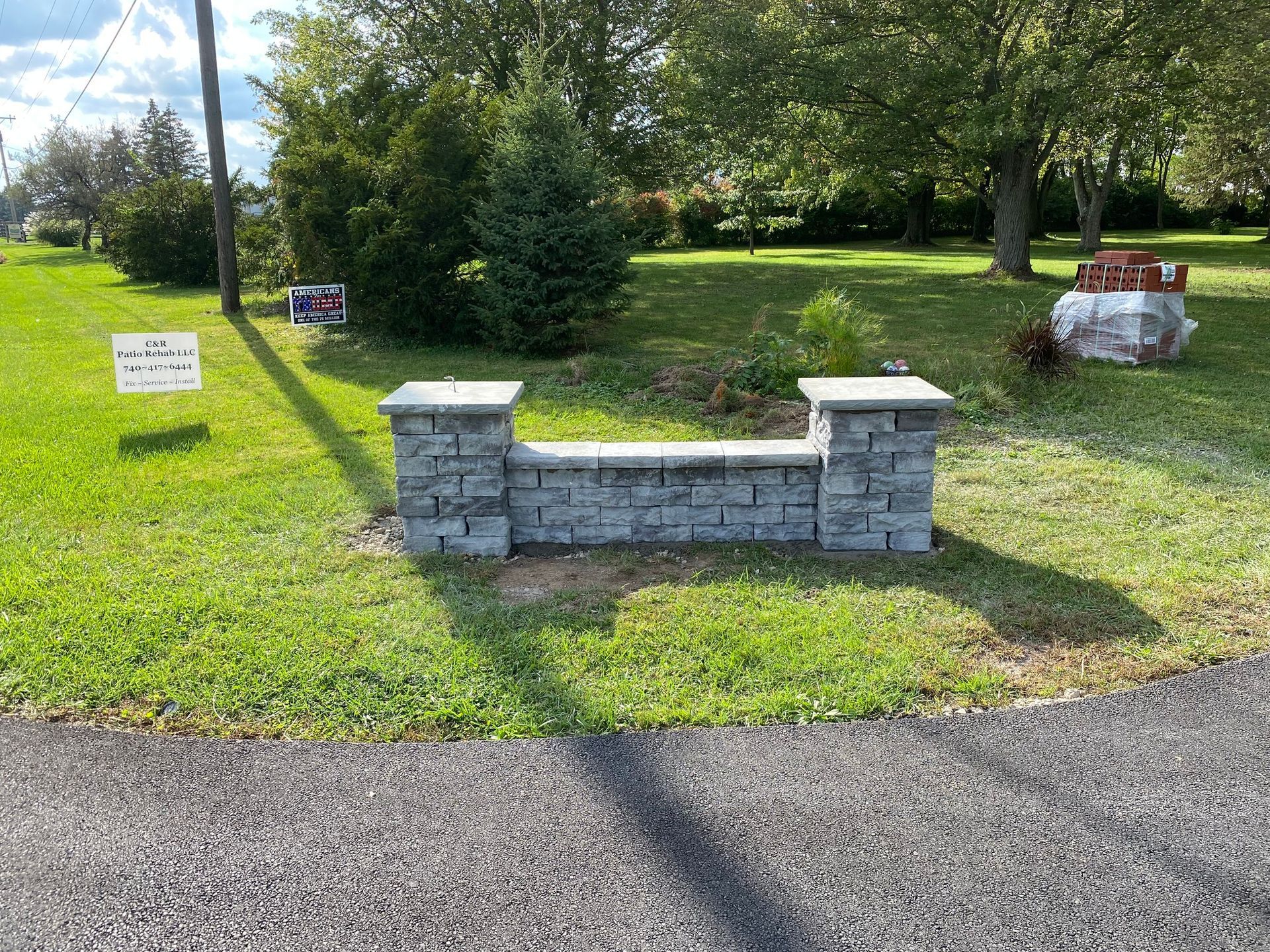 Stone mailbox structure in front yard, gray bricks, green grass, trees in background.