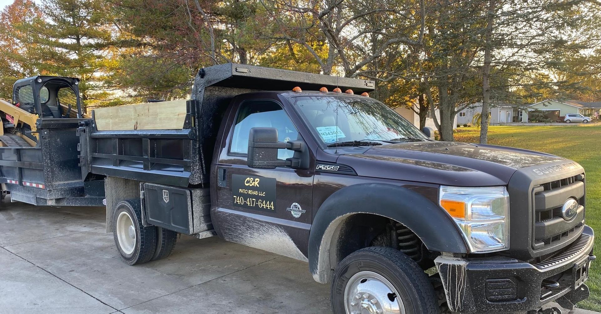 Dark dump truck and trailer with equipment on a residential street.