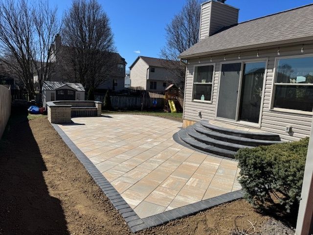 Backyard patio with light pavers, dark border, steps to the house, and a built-in grill area.