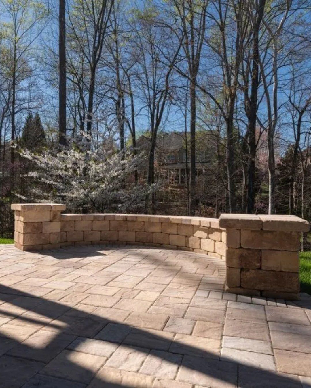 Stone patio with low wall and pillars, surrounded by trees.